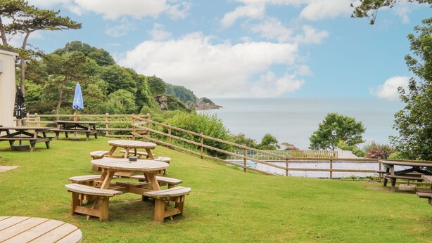 An outdoor dining area with picnic tables and benches, overlooking a body of water and a mountainous landscape. - Ochenta (Ilfracombe)