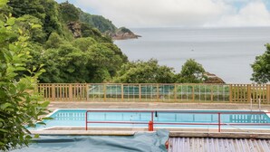 A pool area with a view of the sea and a forested hillside. - Ochenta (Ilfracombe)