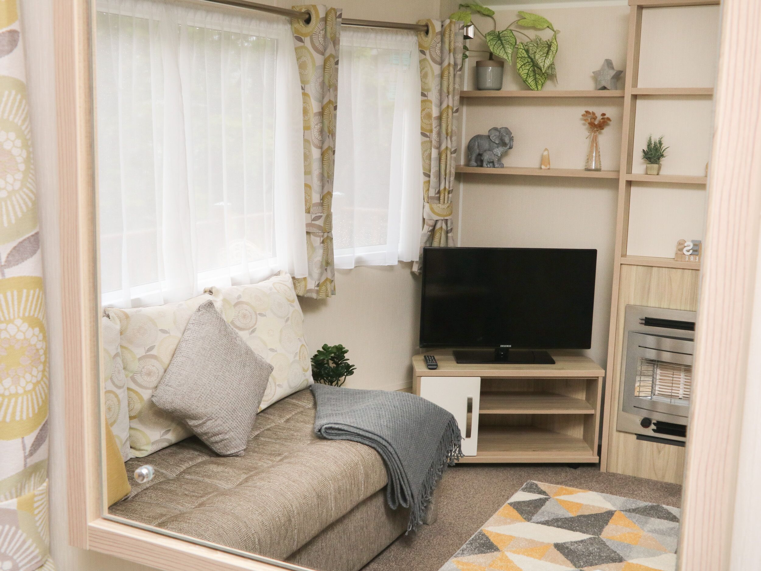 A cozy living room with a sofa, TV, and shelves with decorative items.