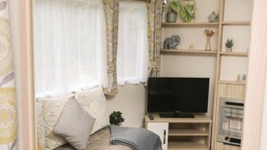 A cozy living room with a sofa, TV, and shelves with decorative items. - Ochenta (Ilfracombe)