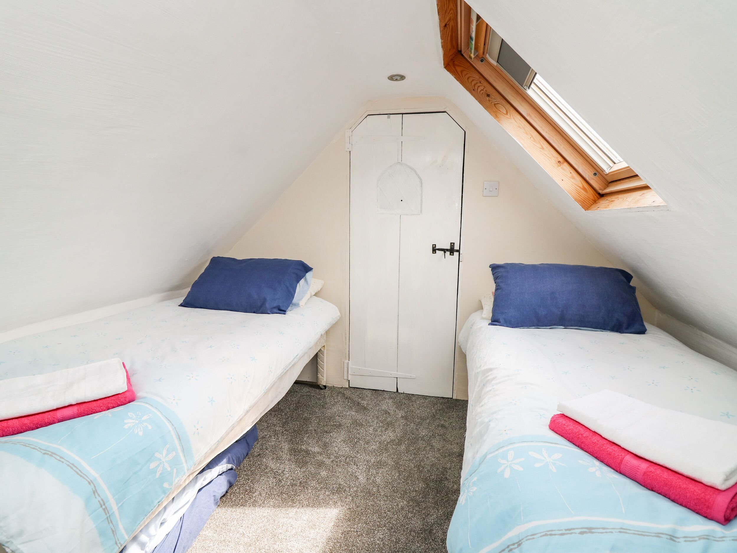 A small, single-room accommodation with two beds, a white door, and a skylight.