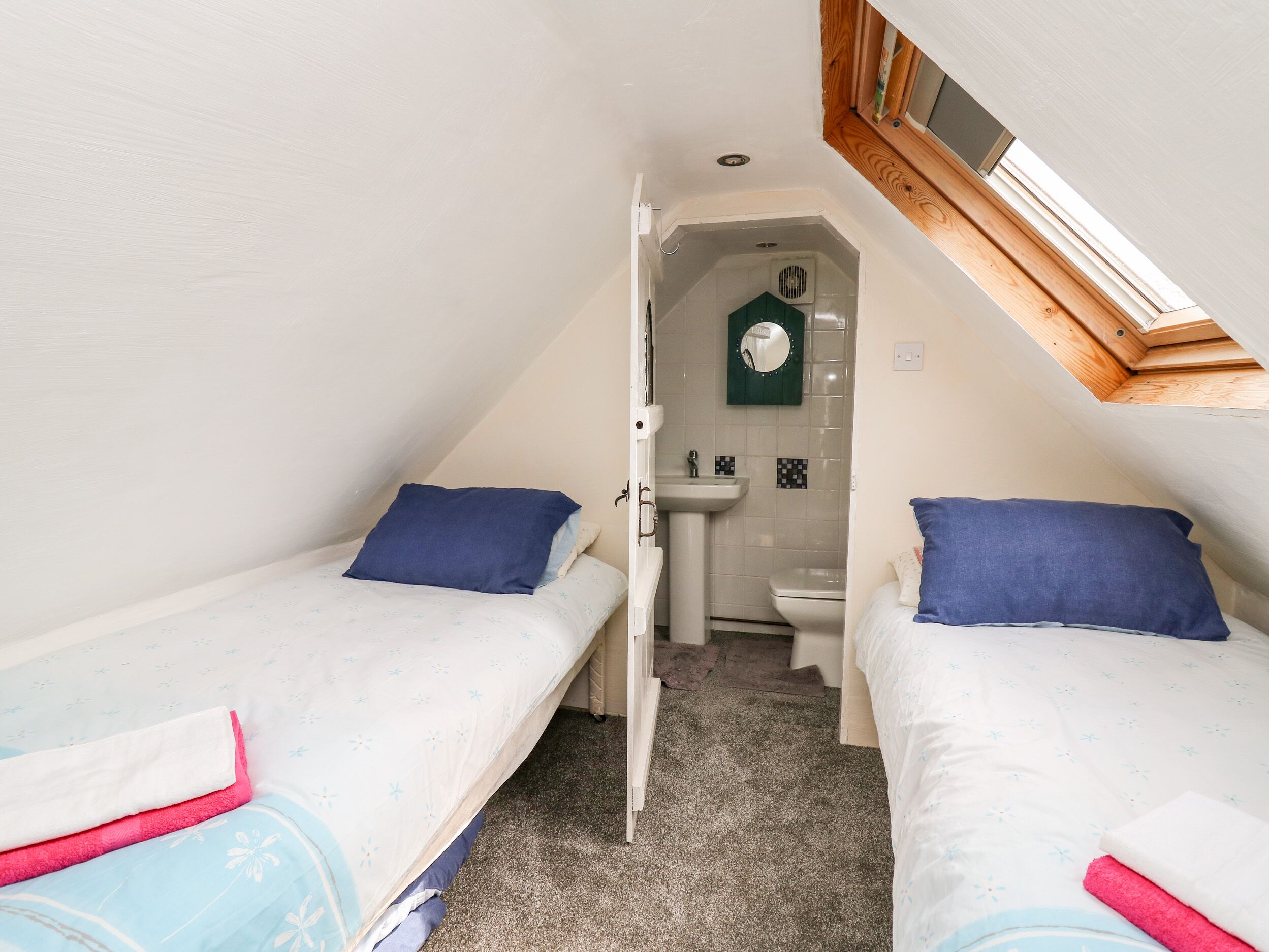 A small, compact room with two single beds, a shared bathroom, and a skylight.