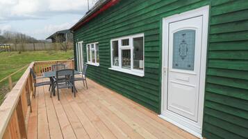 A green house with a wooden deck, a door with a decorative glass panel, and a window with a white frame.