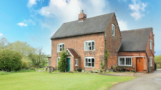 A two-story brick house with a sloped roof, a green door, and a small porch. - The Mill Wheel (Ashbourne)