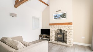 A living room with a stone fireplace, a flat-screen TV, and a beige sofa. - Laurel Farm (Malton)