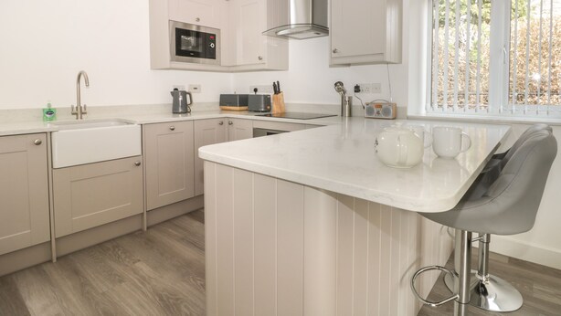 A modern kitchen with a central island, built-in appliances, and a window with a view of trees. - Laurel Farm (Malton)