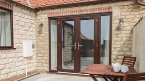 A stone building with a tiled roof, a wooden table with chairs, and a glass door. - Laurel Farm (Malton)