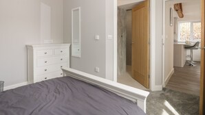 A bedroom with a bed, a dresser, a mirror, and a door leading to a bathroom and a kitchen area. - Laurel Farm (Malton)