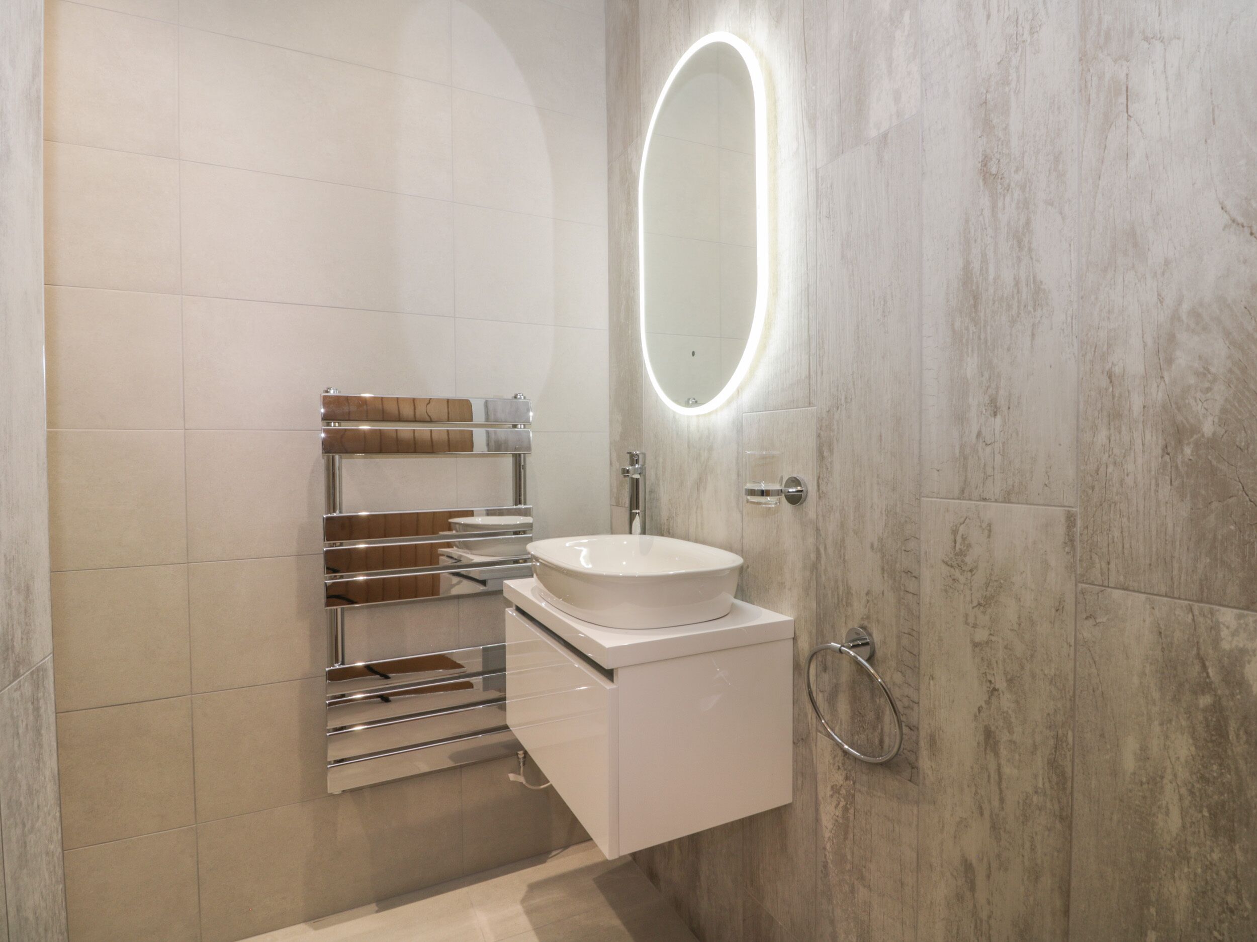 Casa de banho moderna com lavatório branco, toalheiro cromado e espelho com luz embutida.