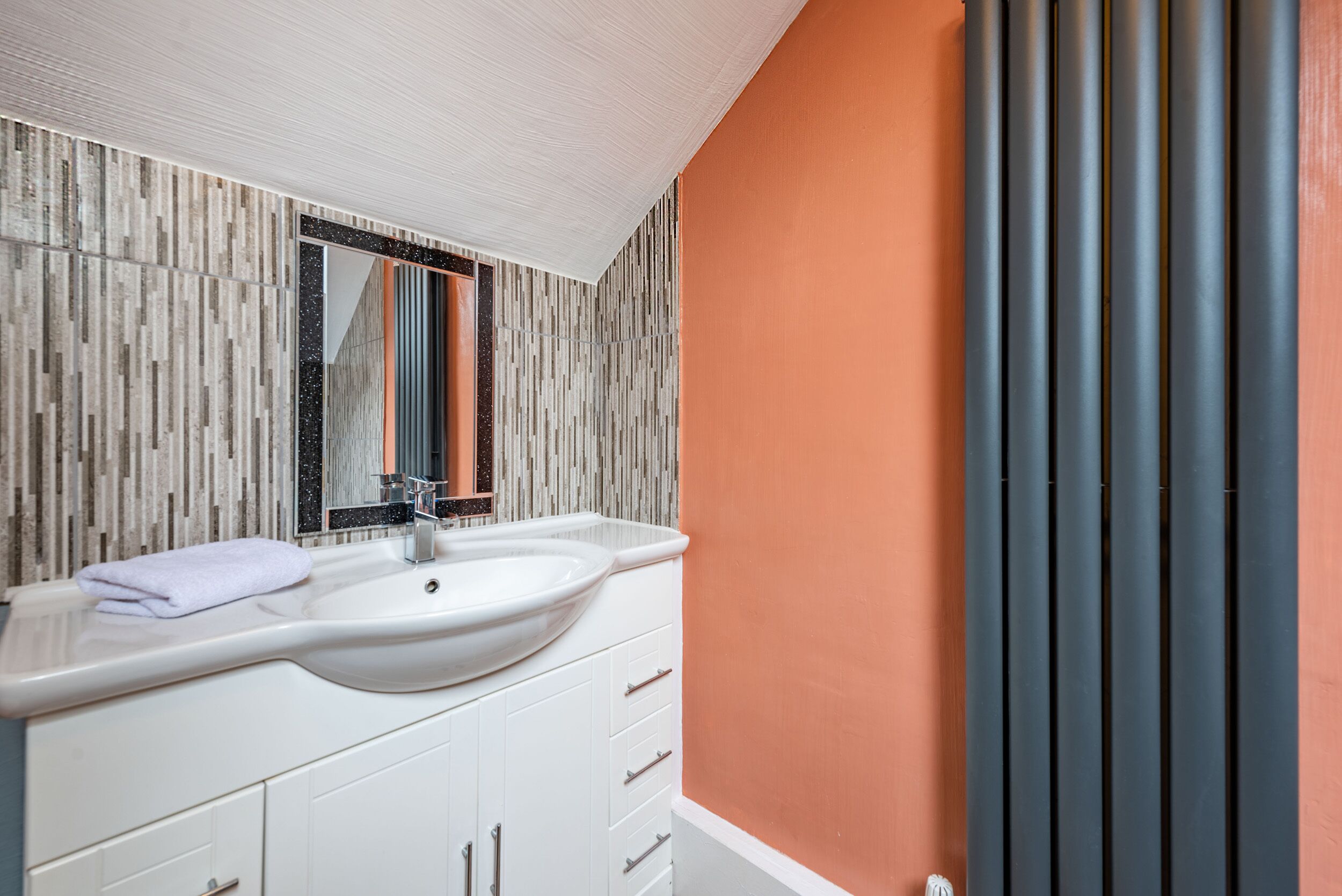 Un baño moderno con un tocador blanco, un espejo grande y una pared con textura.