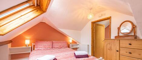A bedroom with a sloped ceiling, a bed with white and red bedding, a wooden dresser, and a mirror.