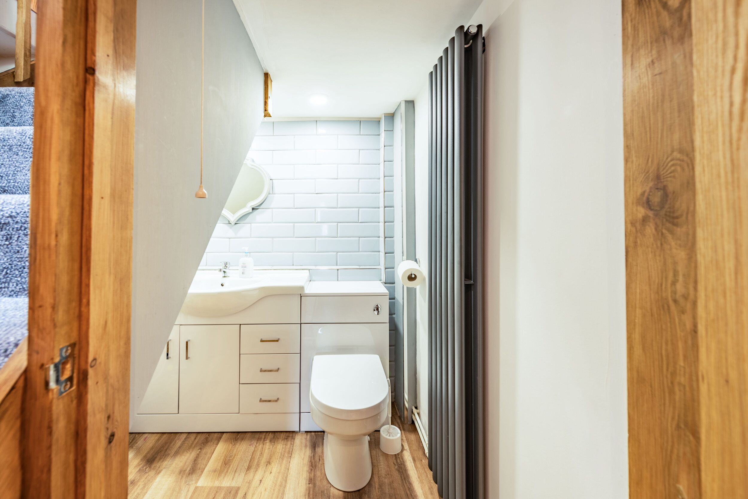Casa de banho compacta com lavatório branco, sanita e soalho em madeira.