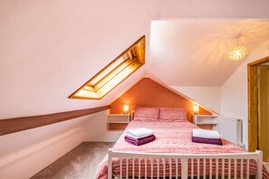 A bedroom with a sloped ceiling, a skylight, a bed with a patterned bedspread, and bedside lamps. - Pendre Cottage (Llanfyrnach)