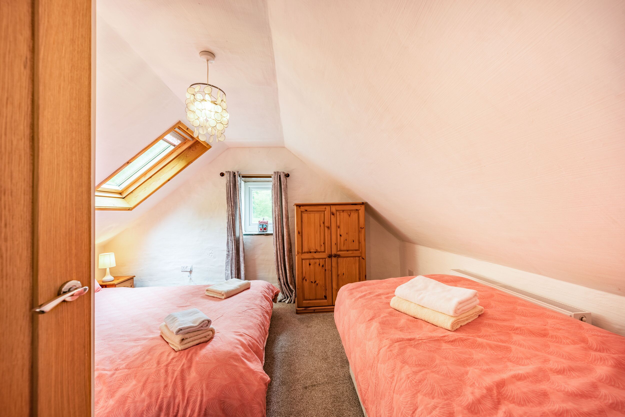A bedroom with two beds, a wooden wardrobe, a skylight, and a ceiling light fixture.