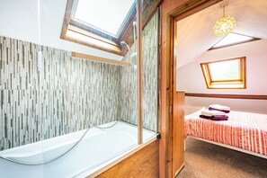 A modern bathroom with a glass bathtub, wooden accents, and a skylight. - Pendre Cottage (Llanfyrnach)