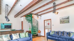 Een woonkamer met twee blauwe banken, een houten vloer, een blauw gestreept tapijt, een groene spiltrap en een spiegel aan de muur.