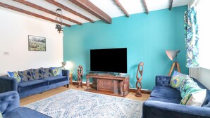 Een woonkamer met een blauwgroene wand, houten balken, een flatscreen televisie, twee banken, een tapijtend en een veren kussen.