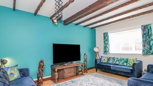 Een woonkamer met turquoise wanden, een houten tv-meubel, een flatscreen-televisie, een blauwe bank en een kamerkleed met dessin.