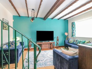 A living room with teal walls, a wooden ceiling, a flat-screen TV, blue sofas, and a patterned rug. - The Brewery (Weymouth)