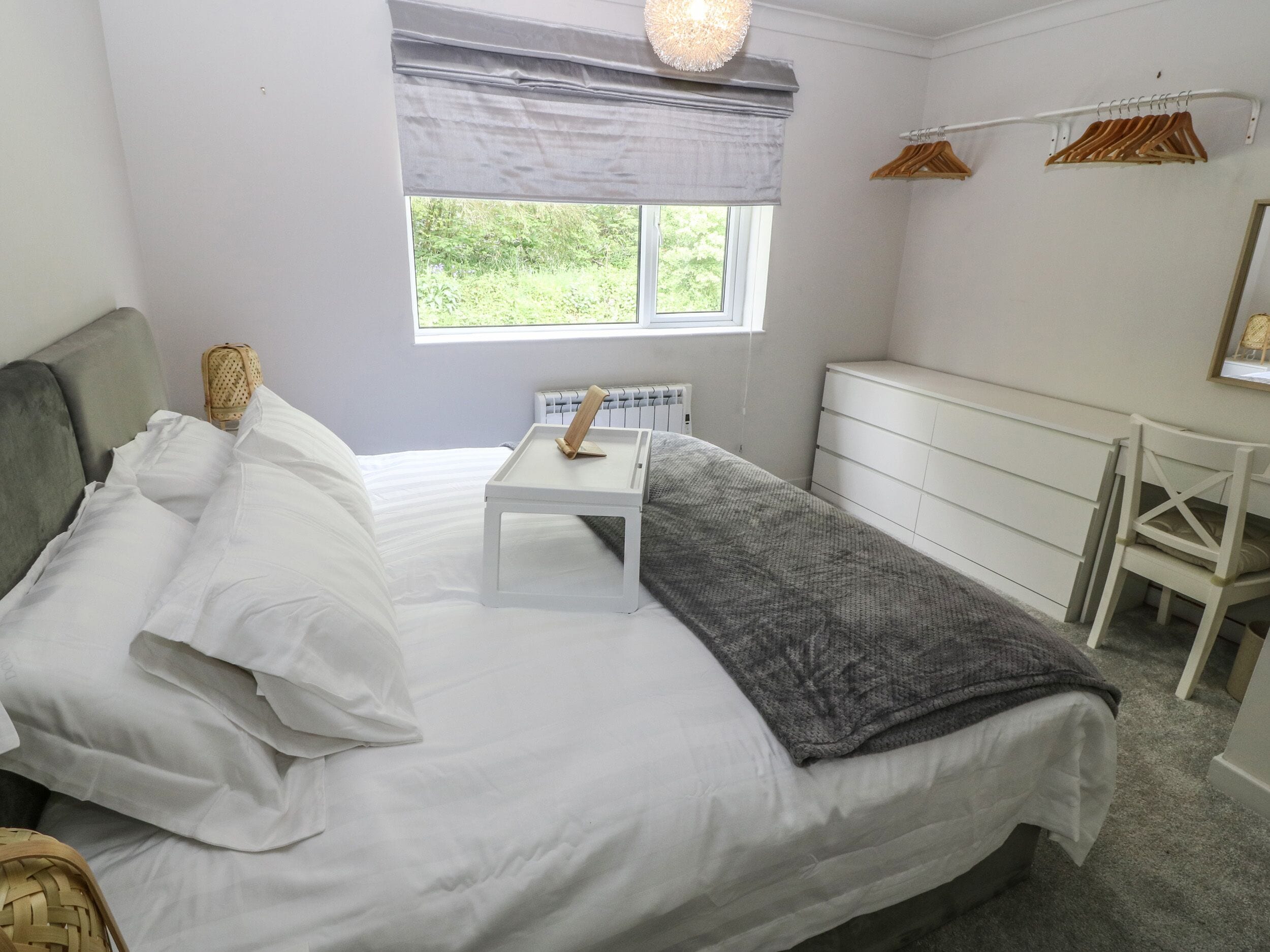 Un dormitorio con cama, mesita de noche, cómoda y ventana con vistas al verdor.