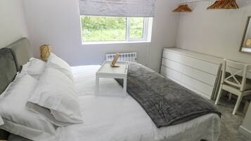 Un dormitorio con cama, mesita de noche, cómoda y ventana con vistas al verdor.