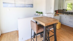 Una cocina moderna con una mesa de madera y taburetes de bar, muebles de color blanco y vistas al mar por la ventana.