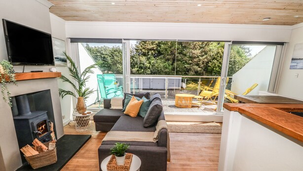 Una sala moderna con chimenea, un sofá, un televisor y un balcón con mobiliario exterior.