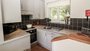 Cocina moderna con armarios blancos, azulejos negros, encimera de granito, horno empotrado, lavamanos y ventana con vistas a la vegetación.