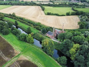 An aerial view of a rural landscape with fields, a river, and a brick building with chimneys. - The Pump House Art Studio (Doncaster)