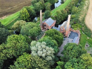 An aerial view of a historic building with two chimneys, surrounded by lush greenery and a small water body. - The Pump House Art Studio (Doncaster)