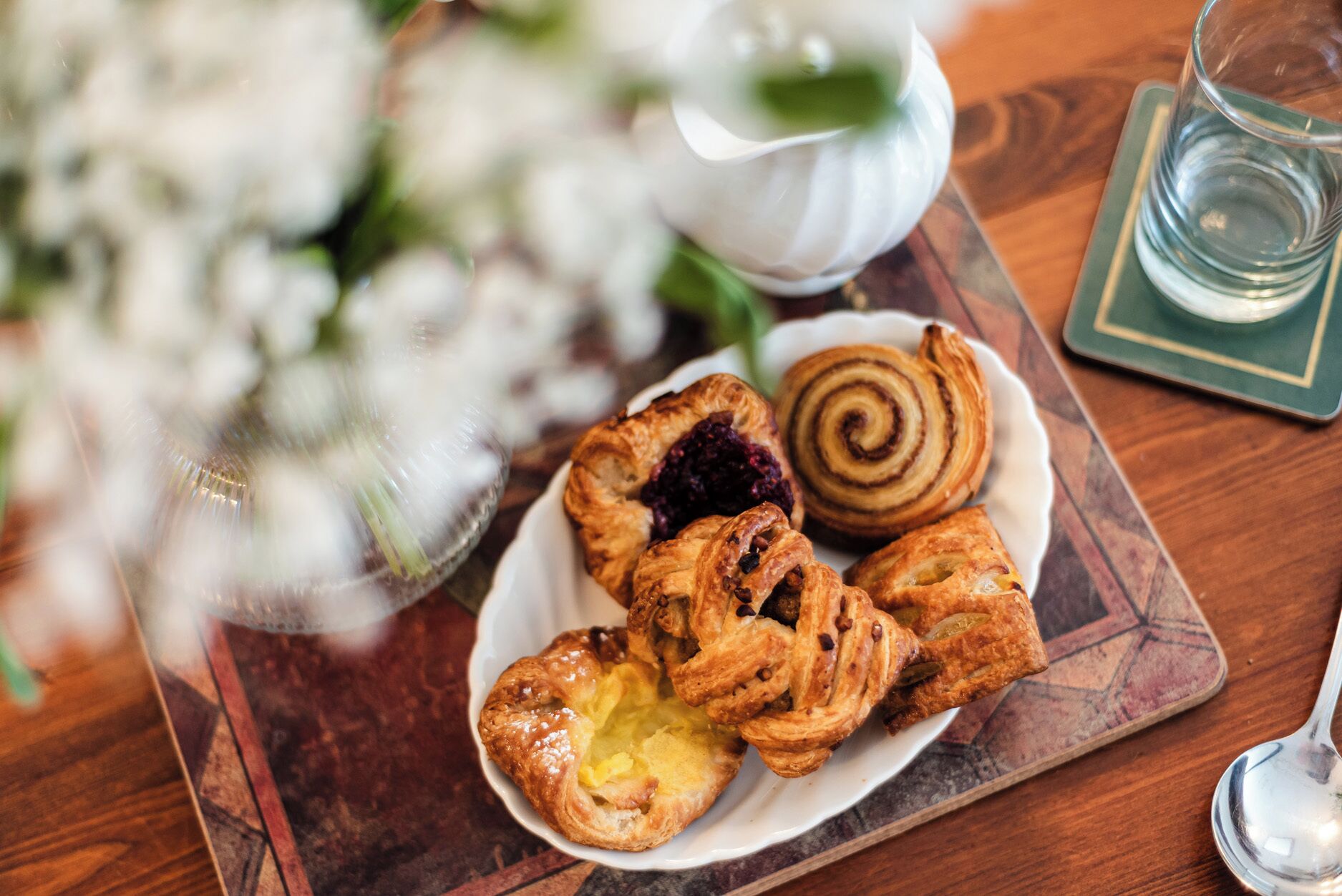 Une assiette de pâtisseries sur une table en bois, avec un verre d’eau et une théière en arrière-plan.
