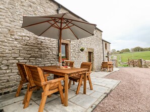 A stone building with a wooden table and chairs, an umbrella, and a bottle of wine. - Owls Barn (Ashbourne)
