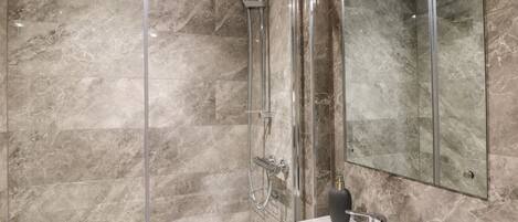A modern bathroom with a glass-enclosed shower, a white sink, and a large mirror.