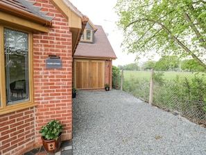 A brick building with a wooden door, a sign reading "GLOBE COTTAGE", and a gravel driveway leading to a fenced area.