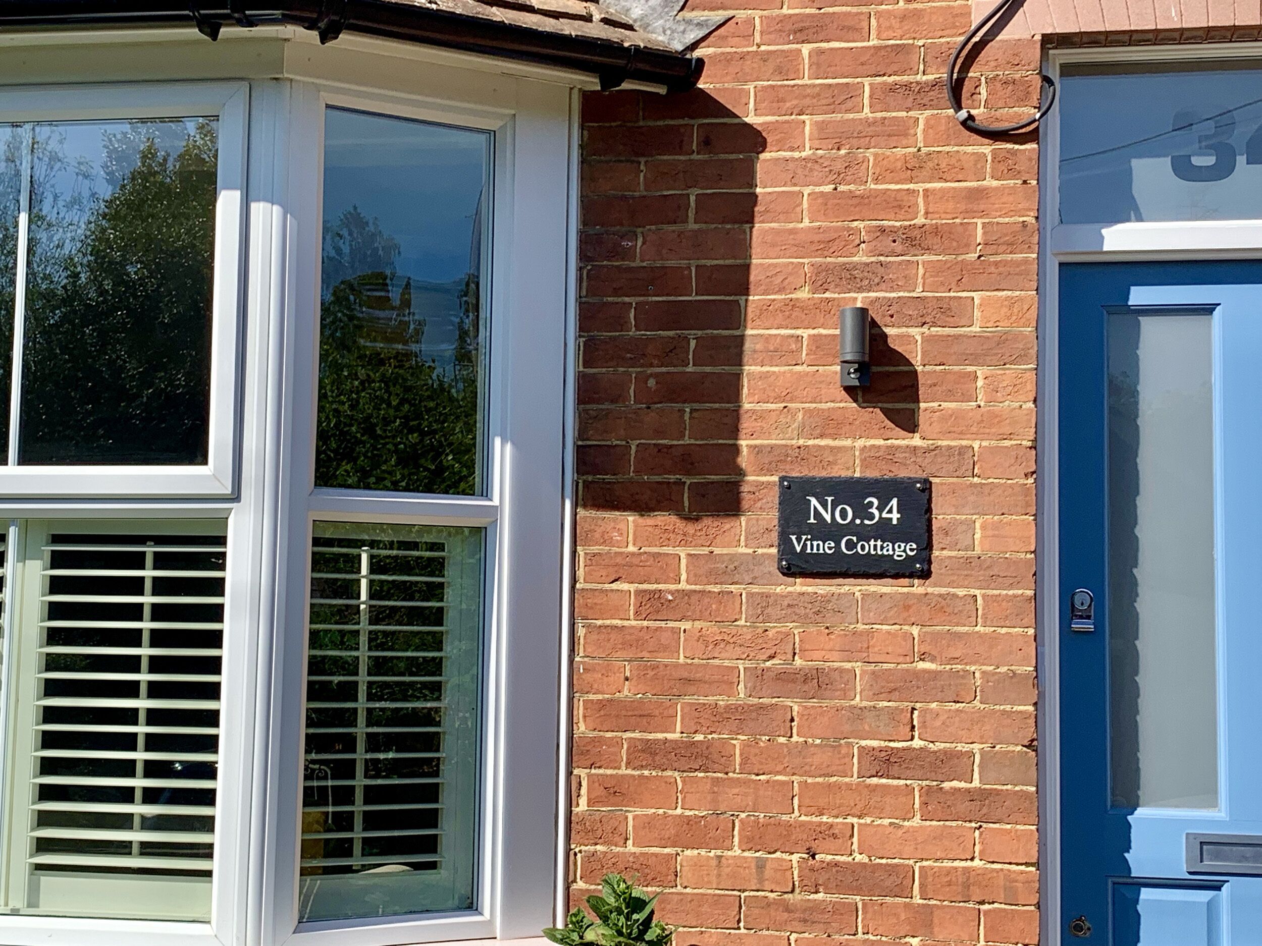A brick house with a blue door, a window with blinds, and a sign reading "No.34 Vine Cottage."