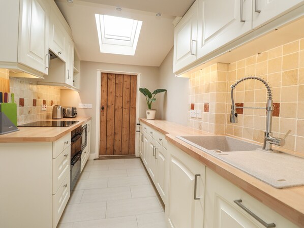 A modern kitchen with white cabinetry, a skylight, a wooden door, a sink with a modern faucet, and a potted plant. - Vine Cottage (Tenterden)