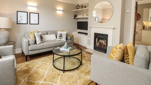 Una sala de estar con un sofá gris, una mesa de centro, una chimenea y un televisor.