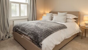 Un dormitorio con una cama, una mesita de noche con lámpara, una ventana con cortinas y un radiador.