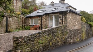 A stone house with a sloped roof, a bench outside, and a stone wall in front. - Horncop Nook (Kendal)