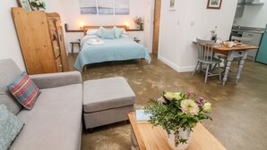 A cozy bedroom with a bed, a wooden wardrobe, a grey sofa, and a small table with a vase of flowers. - Horncop Nook (Kendal)