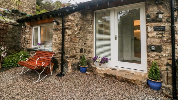 A stone building with a wooden bench and potted plants. - Horncop Nook (Kendal)