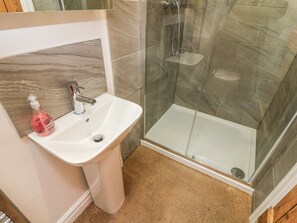 A bathroom with a white sink, a glass shower enclosure, and a marble-tiled wall. - Horncop Nook (Kendal)