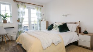 A bedroom with a bed, bedside tables, a desk, a chair, and a window with curtains. - Badgers Way (Tintagel)