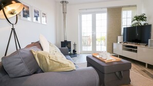 A modern living room with a grey sofa, a floor lamp, a fireplace, a TV, and a balcony with a view. - Badgers Way (Tintagel)