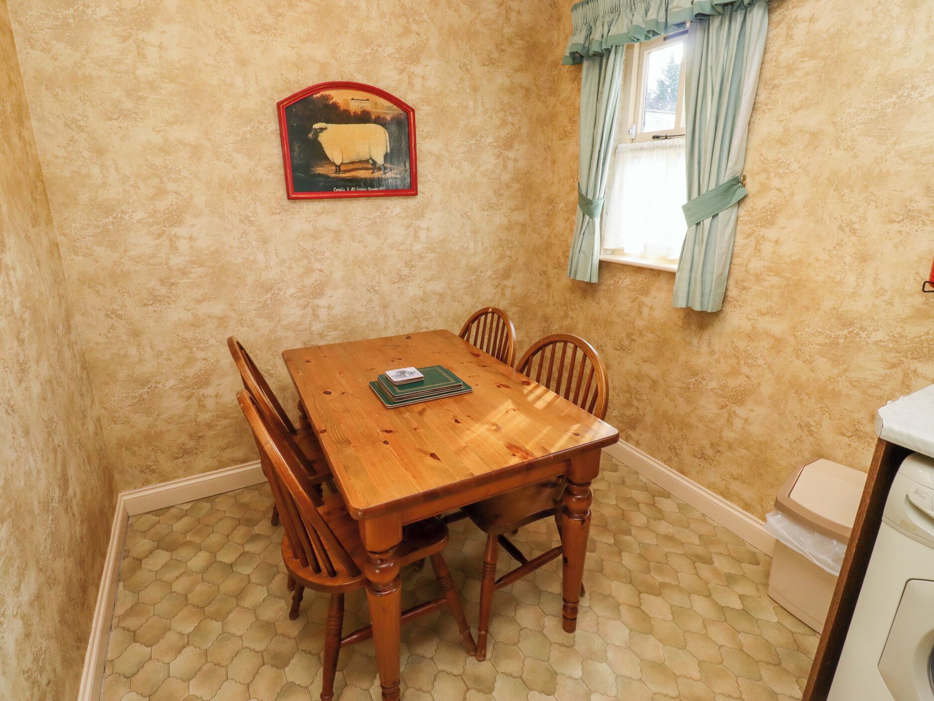 A dining room with a wooden table and chairs, a framed picture on the wall, and a window with curtains.