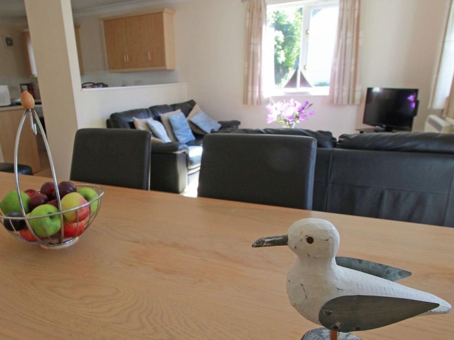 A dining area with a table, chairs, a fruit bowl, and a decorative bird.