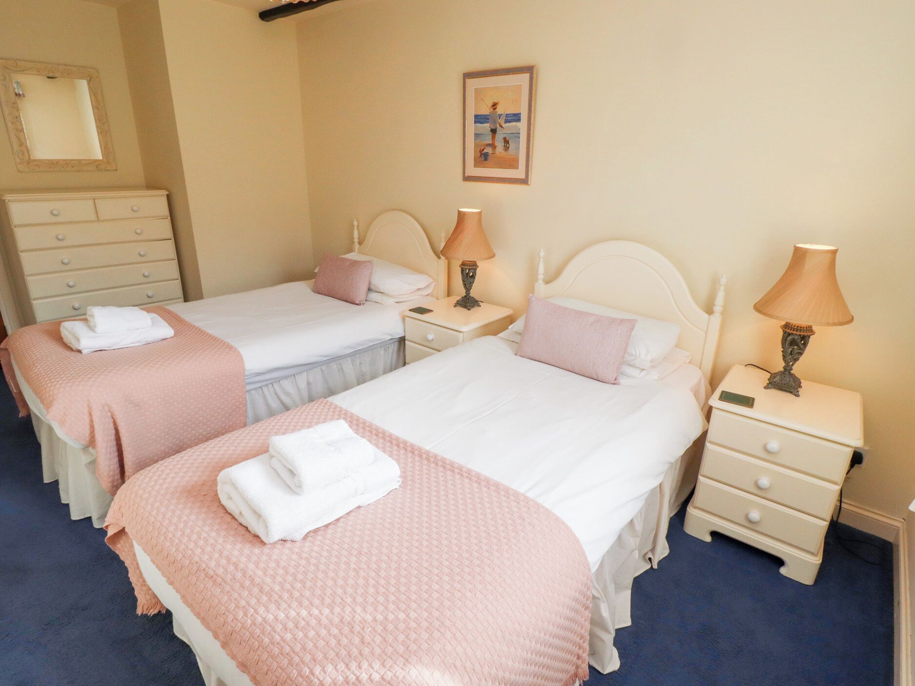 Een hotelkamer met twee bedden, elk voorzien van een nachtkastje, een lamp en een bijzettafeltje. Er is een dressoir en een inlijsting foto aan de muur.