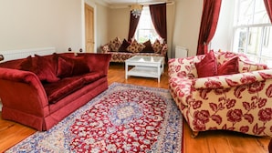 Una sala de estar con un sofá de terciopelo rojo, un sofá estampado, una mesa de centro y una alfombra grande.