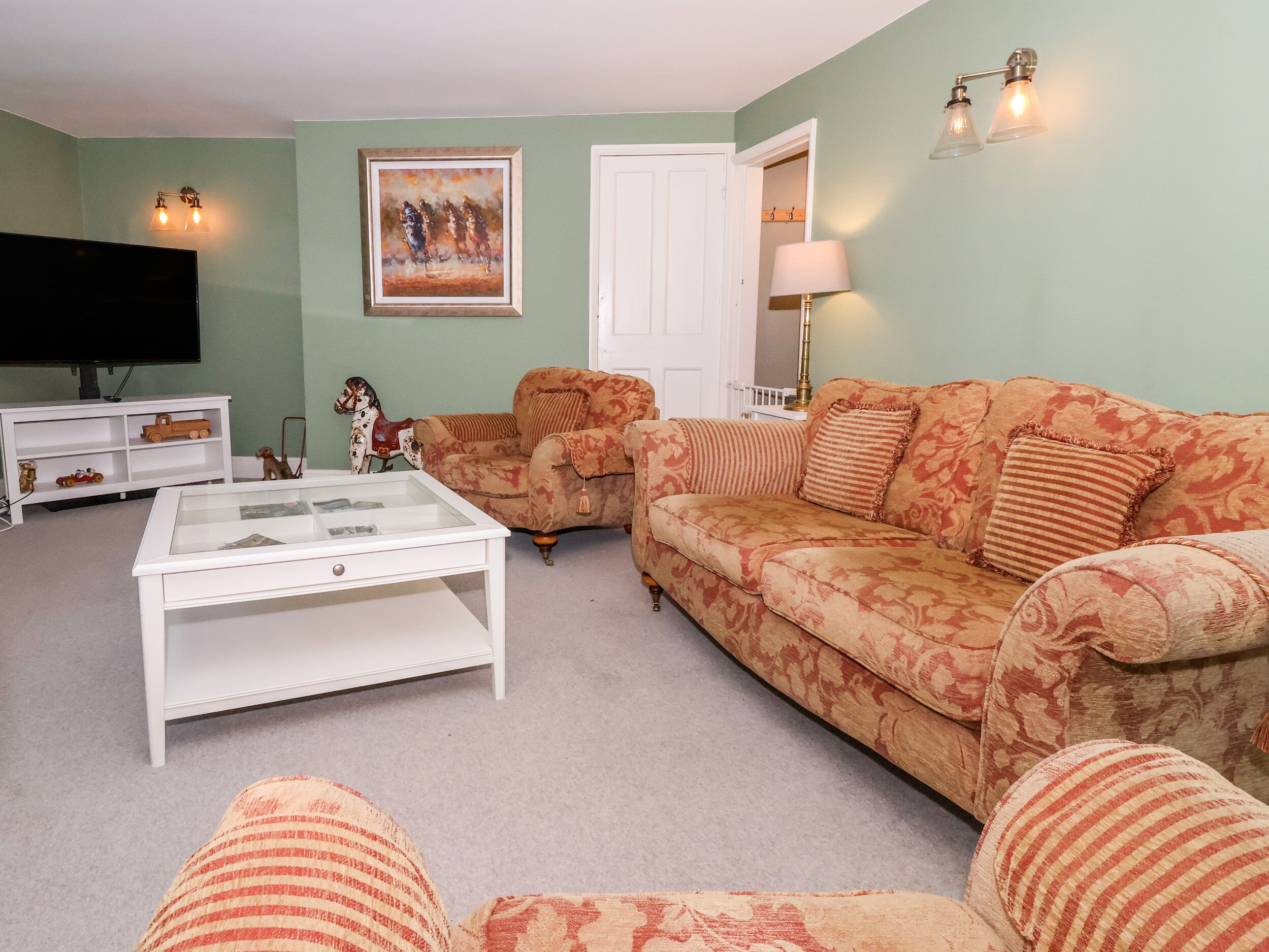 A living room with a sofa, armchairs, a coffee table, a TV, and a painting on the wall.