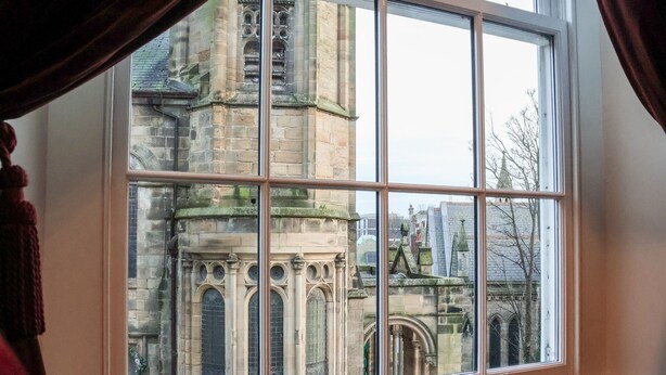 Una ventana con vista a un edificio histórico de ventanas arqueadas y mampostería de piedra.